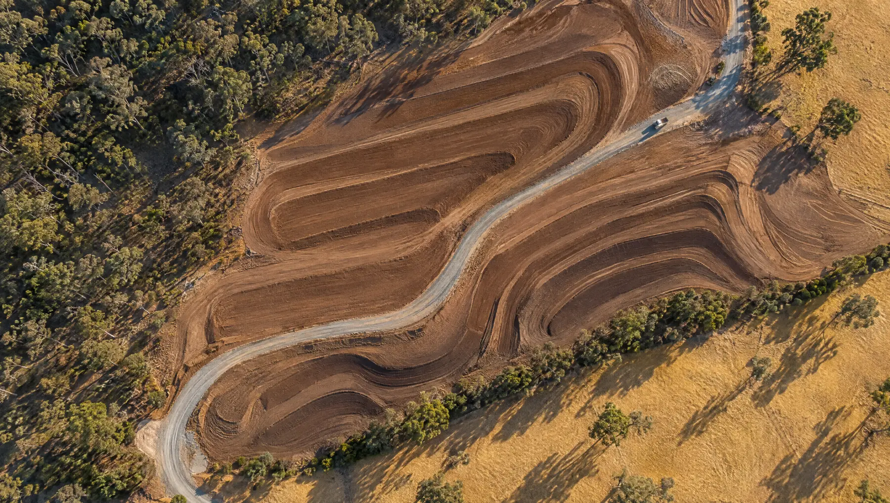 Aerial view of contoured rehabilitation earthworks meeting eucalypt woodland and golden paddocks